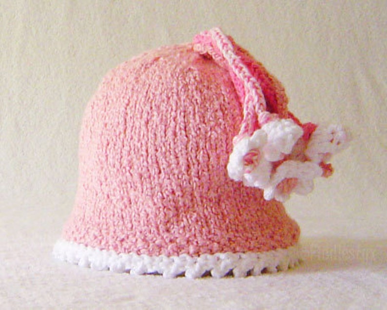 Puede incluir: Un gorro de crochet rosa con un borde blanco de crochet y un adorno de flor de crochet rosa y blanco.