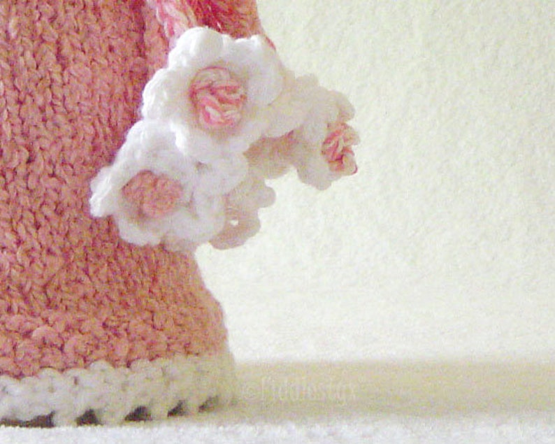 Puede incluir: Un vestido de crochet rosa con flores de crochet blancas alrededor del dobladillo inferior.