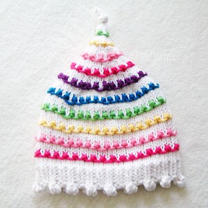 May include: White knitted hat with a rainbow pattern of colorful yarn. The hat has a pointed top and a scalloped brim.