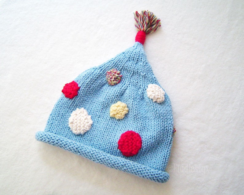May include: A light blue knitted hat with a pom-pom on top and colorful polka dots.