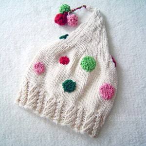 May include: White knitted hat with a red, green and pink polka dot pattern. The hat has a small pom-pom on top.