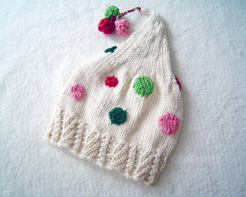 May include: White knitted hat with a red, green and pink polka dot pattern. The hat has a small pom-pom on top.