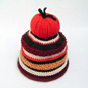 Puede incluir: Un gorro de punto con un dise&ntilde;o en capas en tonos de rojo, naranja, marr&oacute;n y blanco. La capa superior tiene forma de tomate.