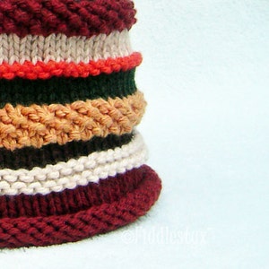 Puede incluir: Un gorro de punto con un patr&oacute;n de rayas burdeos, blanco, naranja, verde y marr&oacute;n.
