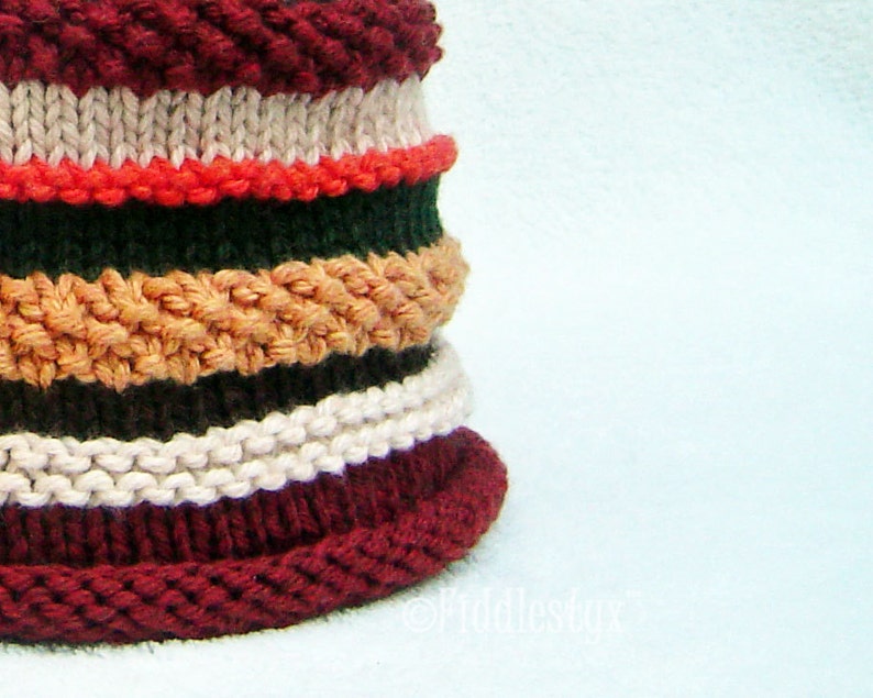 Puede incluir: Un gorro de punto con un patr&oacute;n de rayas burdeos, blanco, naranja, verde y marr&oacute;n.