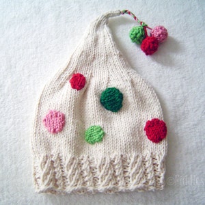 May include: A white knitted hat with a pointed top and a pom-pom on the end. The hat is decorated with colourful polka dots in pink, green, and red.