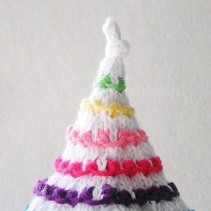 May include: White crocheted hat with a pointed top and colorful stripes of green, yellow, pink, and purple yarn.