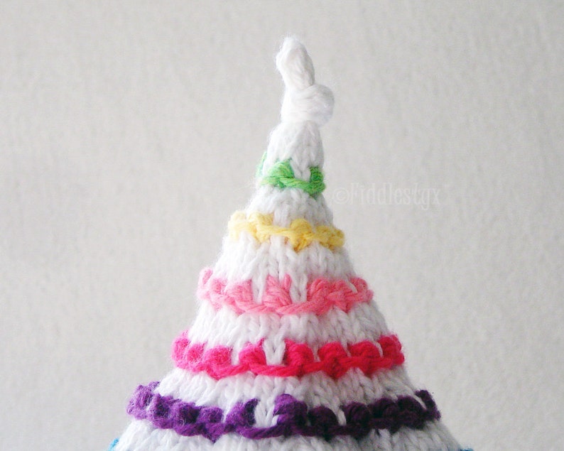 May include: White crocheted hat with a pointed top and colorful stripes of green, yellow, pink, and purple yarn.