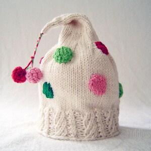 May include: White knitted hat with a pointed top and a long tail. The hat is decorated with colourful polka dots in shades of pink, green, and red.