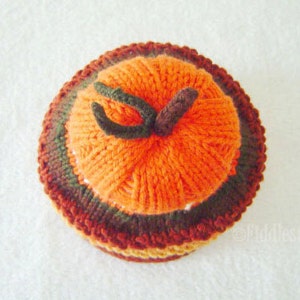 Puede incluir: Un gorro de punto de calabaza con rayas naranjas, marrones y verdes. El gorro est&aacute; hecho de hilo y tiene una superficie texturizada.