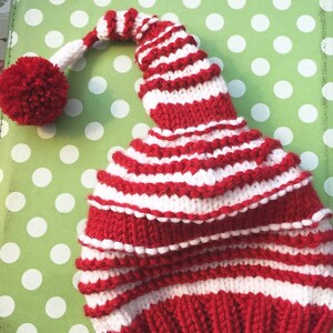 K&ouml;nnte beinhalten: Eine rot-wei&szlig; gestreifte Strickm&uuml;tze mit einem Bommel oben. Die M&uuml;tze hat eine lange, spitze Spitze.