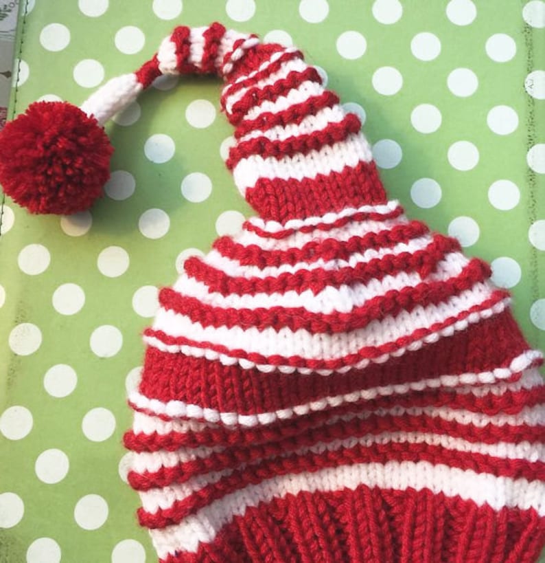 K&ouml;nnte beinhalten: Eine rot-wei&szlig; gestreifte Strickm&uuml;tze mit einem Bommel oben. Die M&uuml;tze hat eine lange, spitze Spitze.