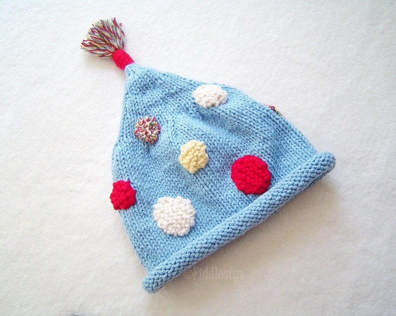 May include: A blue knitted hat with a colorful pom-pom on top. The hat has a variety of colorful felt circles sewn onto it.