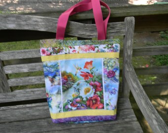 Könnte beinhalten: Eine rosa und gelbe Tragetasche mit einem Blumendruck und einem Kolibri-Design. Die Tasche hat einen gelben, violetten und weißen Besatz.