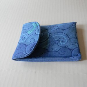 Peut inclure: Un portefeuille en tissu bleu avec un motif de vagues tourbillonnantes. Le portefeuille est plié, révélant un intérieur bleu clair. Le motif présente des nuances de bleu, créant un aspect texturé. Le portefeuille est probablement utilisé pour transporter des cartes et de l'argent.