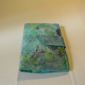 May include: A teal blue fabric wallet with a flap closure. The fabric has a light blue and green watercolor design with starfish and seashells.