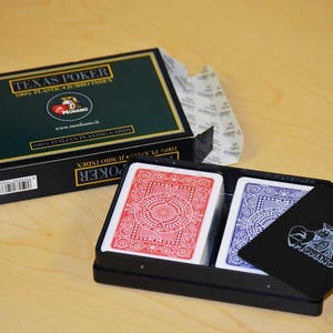 May include: A black box with a deck of playing cards inside. The box has the text "Texas Poker 100% Plastic - Jumbo Index" on the front. The cards are red and blue.