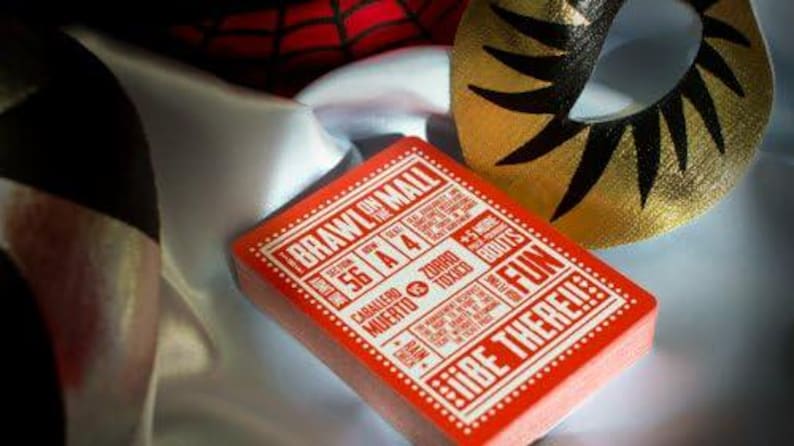 Op de afbeelding: Een rood deck speelkaarten met de woorden "Brawl on the Mall" en "Fun" gedrukt op de voorkant. Het kaartspel ligt op een witte en zwarte stoffen achtergrond.