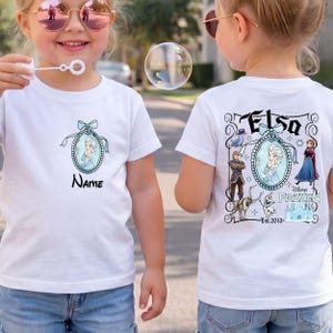 May include: A white short-sleeved t-shirt featuring a small oval graphic of Elsa on the front chest with the text Name below it. The back of the shirt displays a larger Frozen-themed graphic with Elsa, Anna, Kristoff, Sven, Olaf, and a castle.