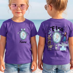 May include: A purple short-sleeved t-shirt featuring a small oval graphic of Elsa on the front with the text Name. The back displays a large graphic with Elsa, Anna, Kristoff, Sven, and Olaf, the text Elsa, Disney Frozen, and Est. 2013.