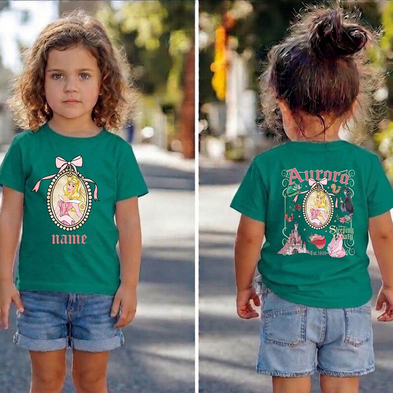 Puede incluir: Una camiseta verde azulado con un dise&ntilde;o de princesa y un campo de nombre. El dise&ntilde;o frontal incluye una princesa con un vestido rosa dentro de un marco ovalado con un lazo. La parte posterior de la camiseta tiene el texto "Aurora Sleeping Beauty" con gr&aacute;ficos adicionales.