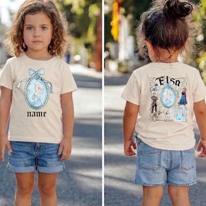 Puede incluir: Camiseta de color beige claro con una imagen de dibujos animados de Elsa de Frozen. La parte delantera de la camiseta tiene un retrato de Elsa con la palabra "name" debajo. La parte trasera de la camiseta tiene la palabra "Elsa" y otros personajes de la pel&iacute;cula.