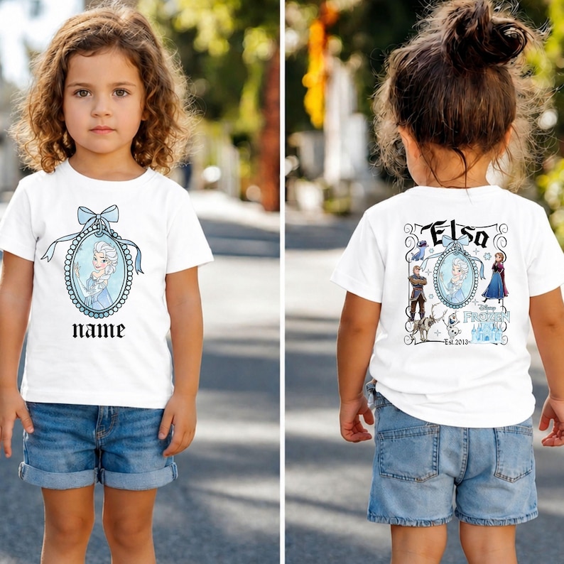 Puede incluir: Camiseta blanca con una imagen de dibujos animados de Elsa de Frozen, enmarcada en un &oacute;valo azul con un lazo. La palabra "name" est&aacute; impresa debajo. La parte posterior de la camiseta tiene la palabra "Elsa" y otros personajes de Frozen.