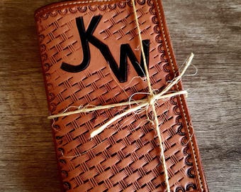 May include: A brown leather wallet with a woven pattern and the initials "KW" in black. The wallet is tied with twine and has a decorative border. The wallet is on a wooden surface.