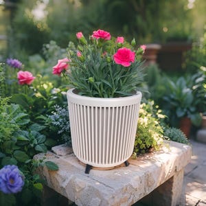 May include: A white, vertically-slatted planter pot with a cream-colored rim, holding vibrant pink carnations. The pot sits on a stone bench in a garden setting, showcasing a blend of natural elements and modern design.