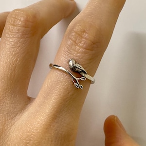 Peut inclure: Bague argentée représentant un oiseau perché sur une branche. La bague entoure le doigt, avec l'oiseau et la branche sur le dessus. La bague est en métal brillant et présente un motif détaillé d'oiseau et de feuilles.
