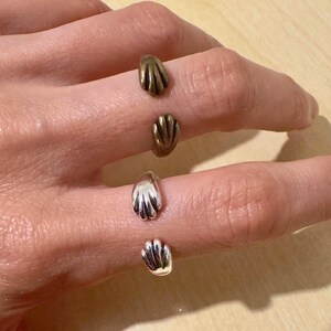 May include: A hand displaying three finger rings. Two rings are bronze, and the other two are silver. Each ring has a small, stylized hand design, offering a unique and artistic aesthetic.