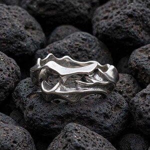 Peut inclure: Une bague en argent au design complexe, organique et fluide, présentant de multiples saillies ondulées superposées et des rainures profondes qui créent un aspect sculptural à fort contraste sur toute la surface de l'anneau en métal.