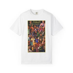 May include: White t-shirt with a colourful collage of people and the text "Abbott Elementary" in yellow. The design is centred on the shirt, displaying a variety of individuals in a vibrant arrangement. The shirt has a classic crew neck.