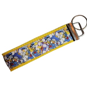 May include: Yellow and white key chain with a blue and white cartoon character print. The key chain has a silver metal ring and a silver metal clasp.