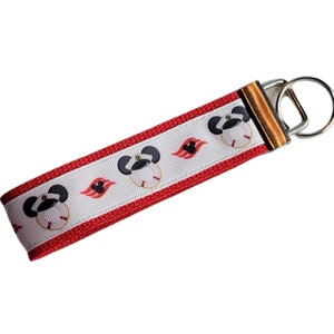 May include: Red and white key chain with a white stripe and a red stripe. The white stripe has a repeating pattern of a black and white Mickey Mouse head wearing a captain's hat and a red and white Disney cruise line logo.