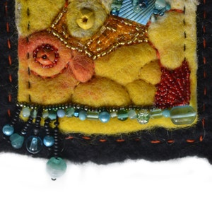 May include: A small, square, yellow felt piece with a variety of colourful beads and embroidery. The felt is stitched with black thread and has a black border. The piece has a fringe of black and blue beads.
