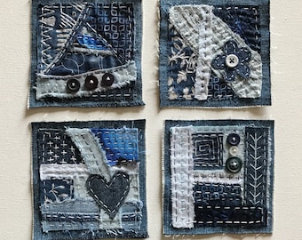 Pode incluir: Quatro quadrados de brim azul com diferentes designs de patchwork e vários botões. Cada quadrado tem um padrão diferente de costura e tecido.