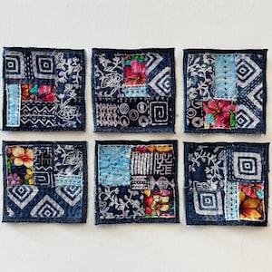 May include: Six handmade fabric squares with a patchwork design. Each square is made of different fabrics with floral, geometric, and abstract patterns in shades of blue, white, and pink. The squares are sewn together with a denim border.