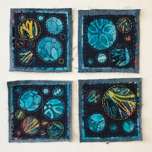 May include: Four square denim-framed art pieces with a dark blue background and colorful circular designs. Each piece features a different arrangement of circles with various patterns and colors, including blue, yellow, and orange.