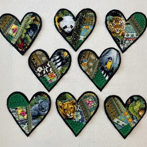 May include: Eight handmade felt heart-shaped patches with a variety of animal and nature designs. The patches are green, black, and brown with a patchwork design.