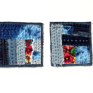 May include: Two square fabric coasters featuring a patchwork design of blue denim strips and floral patterned fabric. The pieces are joined with visible white and red running stitch embroidery, creating a textured, layered appearance on each coaster.