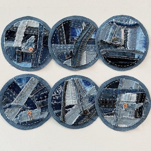 May include: Six round blue denim coasters with a patchwork design. Each coaster is made of different pieces of denim fabric sewn together.
