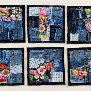 May include: Six square denim patchwork wall hangings with floral embroidery. Each piece features a different arrangement of blue denim fabric scraps, stitched together with contrasting thread. The floral embroidery is done in shades of pink, red, and yellow.