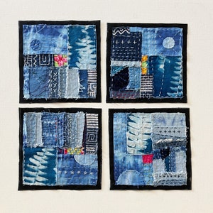 May include: Four square blue and white fabric wall hangings with a patchwork design. Each square is framed with a black border.