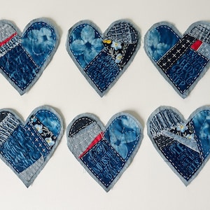 May include: Six heart-shaped fabric patches featuring blue patchwork designs with visible white stitching. The fabric includes floral patterns, denim textures, and text fragments such as "always see it impossible until it is done" and "every journey needs first step."