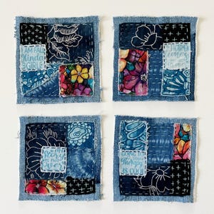 May include: Four square fabric coasters featuring a patchwork design of blue denim, floral patterns, and tie-dye fabric. Each coaster includes white hand-stitched embroidery and patches with text such as "I am fall kinda girl" and "My story is not over."