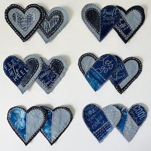 May include: Six pairs of heart-shaped fabric patches made from various shades of blue denim. Each heart features layered stitching, patchwork designs, and printed text including phrases like "FEEL TO HEEL," "BUILT FROM," "LET'S GO," and "COOL MIND."