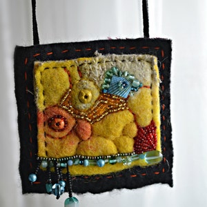 May include: A yellow, orange and blue felt pendant with beads and a black cord. The pendant is a square shape with a stitched border.