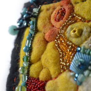 May include: A close-up of a colourful felt and bead artwork. The artwork features a yellow background with orange, red, and blue beads. The beads are arranged in a pattern that resembles a flower.