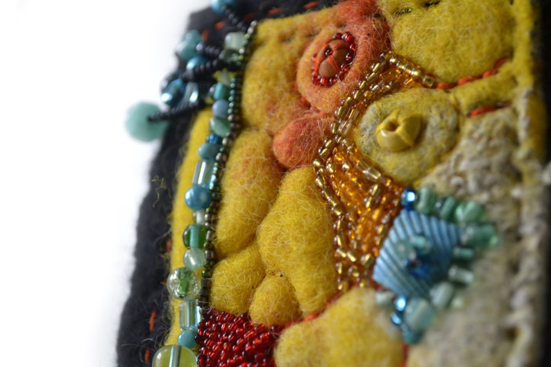 May include: A close-up of a colourful felt and bead artwork. The artwork features a yellow background with orange, red, and blue beads. The beads are arranged in a pattern that resembles a flower.